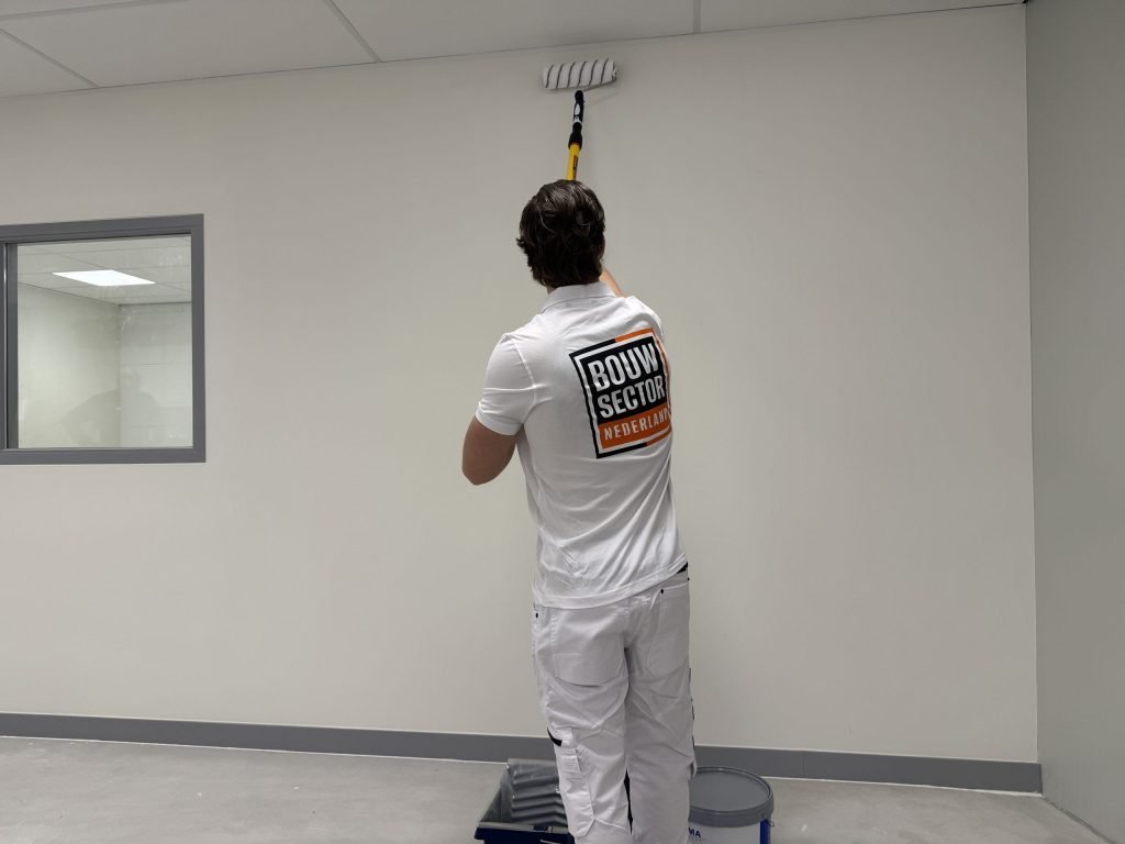 Schilder rolt met een verlengsteel de bovenkant van een lichte wand tot vlak onder het plafond