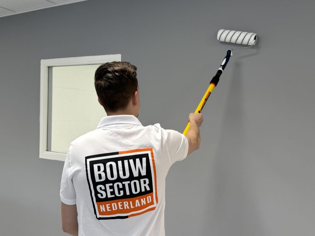 Schilder met het logo van Bouwsector Nederland op zijn rug rolt een grijze muur naast een raam