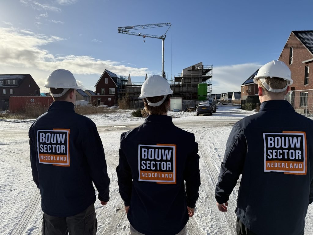 Drie medewerkers van Bouwsector Nederland met witte helm op een besneeuwde straat met bakstenen huizen
