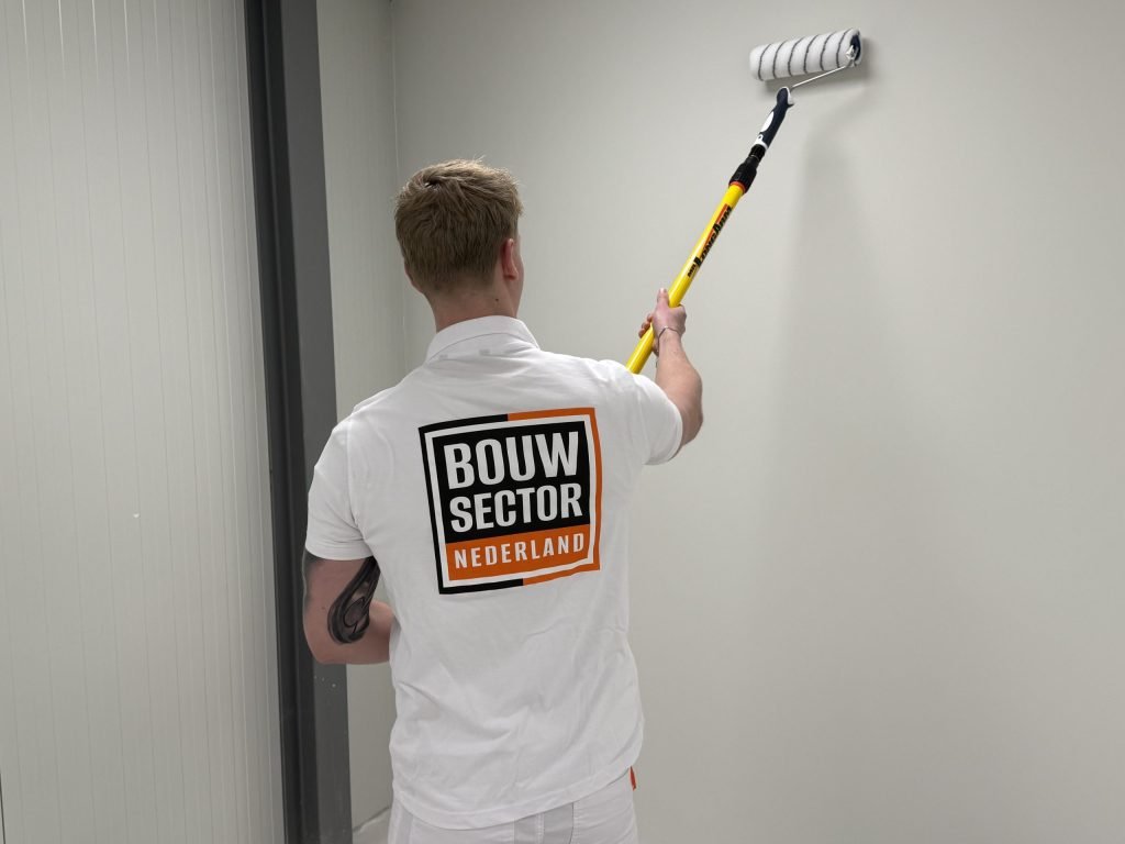 Schilder van Bouwsector Nederland rolt met een telescoopsteel een lichte wand tot vlak onder het plafond